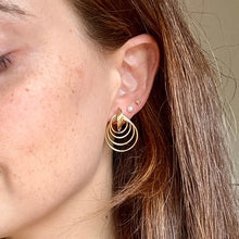 Load image into Gallery viewer, Close-up of a woman wearing gold hoop earrings with a neutral background
