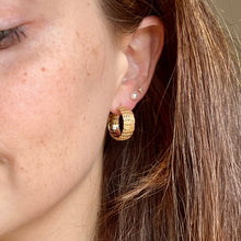 Load image into Gallery viewer, Close-up of a woman wearing gold hoop earrings with a neutral background