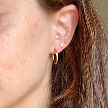 Load image into Gallery viewer, Close-up of a woman wearing gold hoop earrings with a neutral background