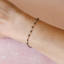 Load image into Gallery viewer, A delicate gold and black bead bracelet worn on a wrist against a pink background