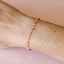 Load image into Gallery viewer, A delicate gold and light pink bead bracelet worn on a wrist against a pink background