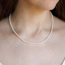 Load image into Gallery viewer, A close-up of a woman wearing a delicate white pearl necklace.