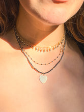 Load image into Gallery viewer, A close-up of a person's neck wearing multiple necklaces. The set includes a short choker with dangling gold-toned beads, a middle beaded chain, and a longer chain with a small gold heart-shaped pendant.