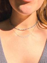Load image into Gallery viewer, A close-up lifestyle shot of a model wearing two necklaces. The top necklace is a varied blue pearls, and the bottom necklace is a delicate white gold and diamond double helix design.