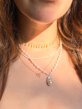Load image into Gallery viewer, A close-up of a person's neck and chest wearing a layered necklace set. The set includes a delicate gold choker with small dangling charms, a strand of white baroque pearls, a gold chain with a small pendant, and a larger pearl necklace with a teardrop-shaped white pearl pendant.