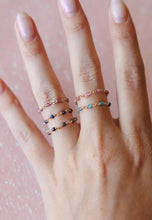 Load image into Gallery viewer, Five delicate wire-wrapped gemstone rings in gold-tone wire, featuring faceted pink, blue, turquoise, and dark gray stones arranged on a hand with a soft pink background.