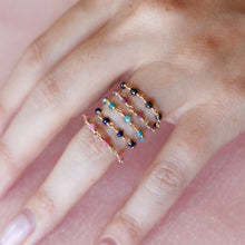 Load image into Gallery viewer, Five delicate wire-wrapped gemstone rings in gold-tone wire, featuring faceted pink, blue, turquoise, and dark gray stones arranged on a hand with a soft pink background.